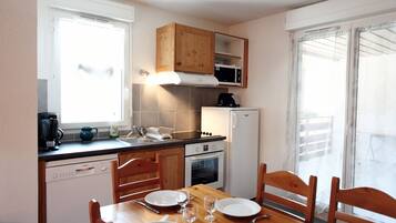 A compact kitchen with wooden cabinets, a microwave, a dishwasher, and a dining table set for four.