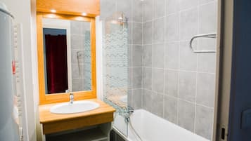A bathroom with a wooden vanity, a white sink, a mirror, a shower with a glass door, and grey tiled walls.