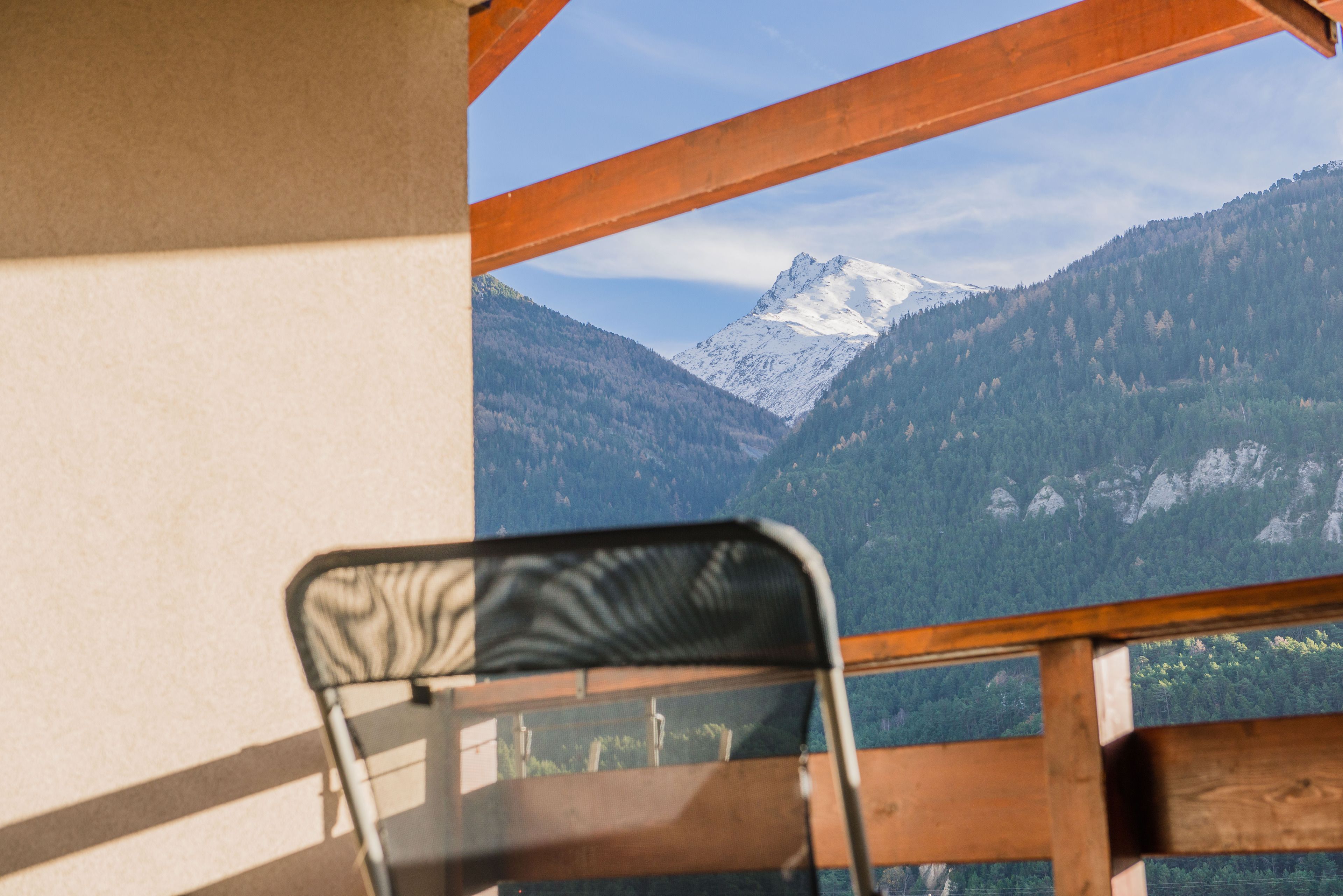 A wooden-framed window with a view of a snow-capped mountain and forested hills.