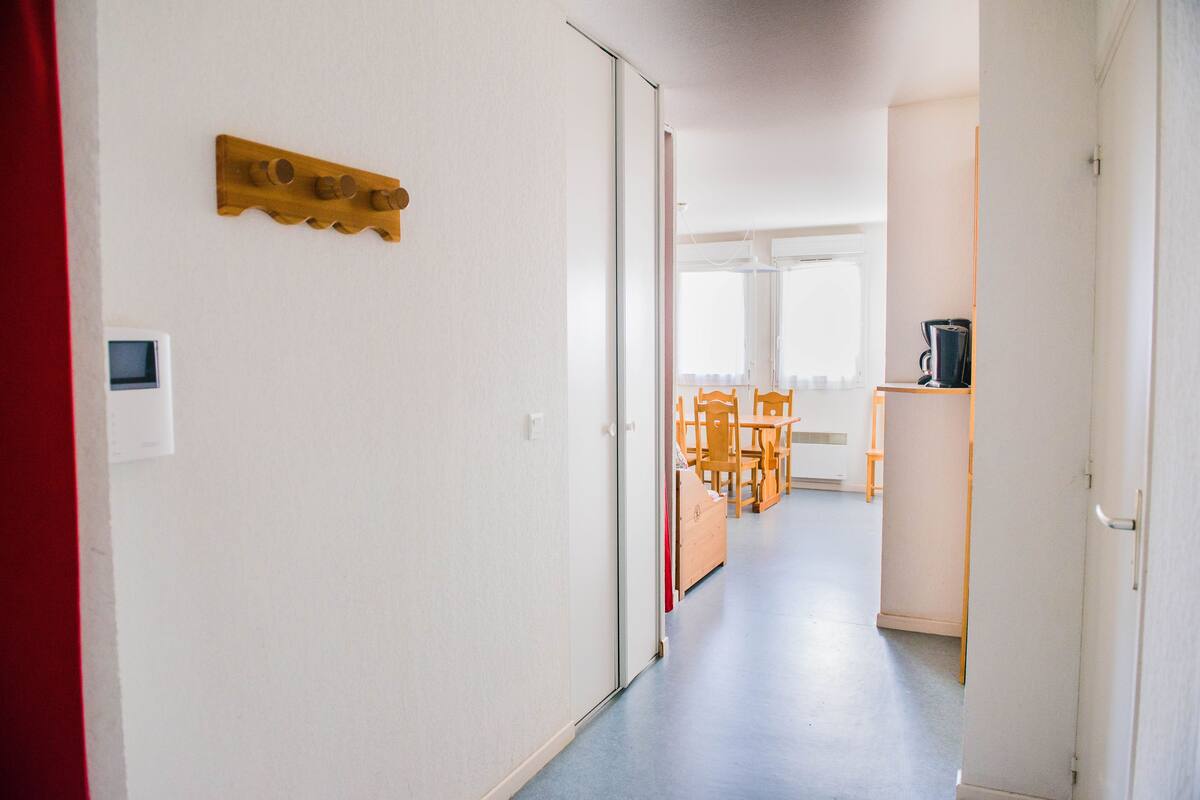 Un couloir orné d’un décor mural en bois, un coin repas avec des chaises et une table en bois, et un espace cuisine équipé d’un réfrigérateur et d’une machine à café.
