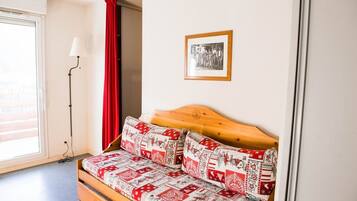 A room with a wooden bed, red and white patterned bedding, a framed picture on the wall, and a red curtain.
