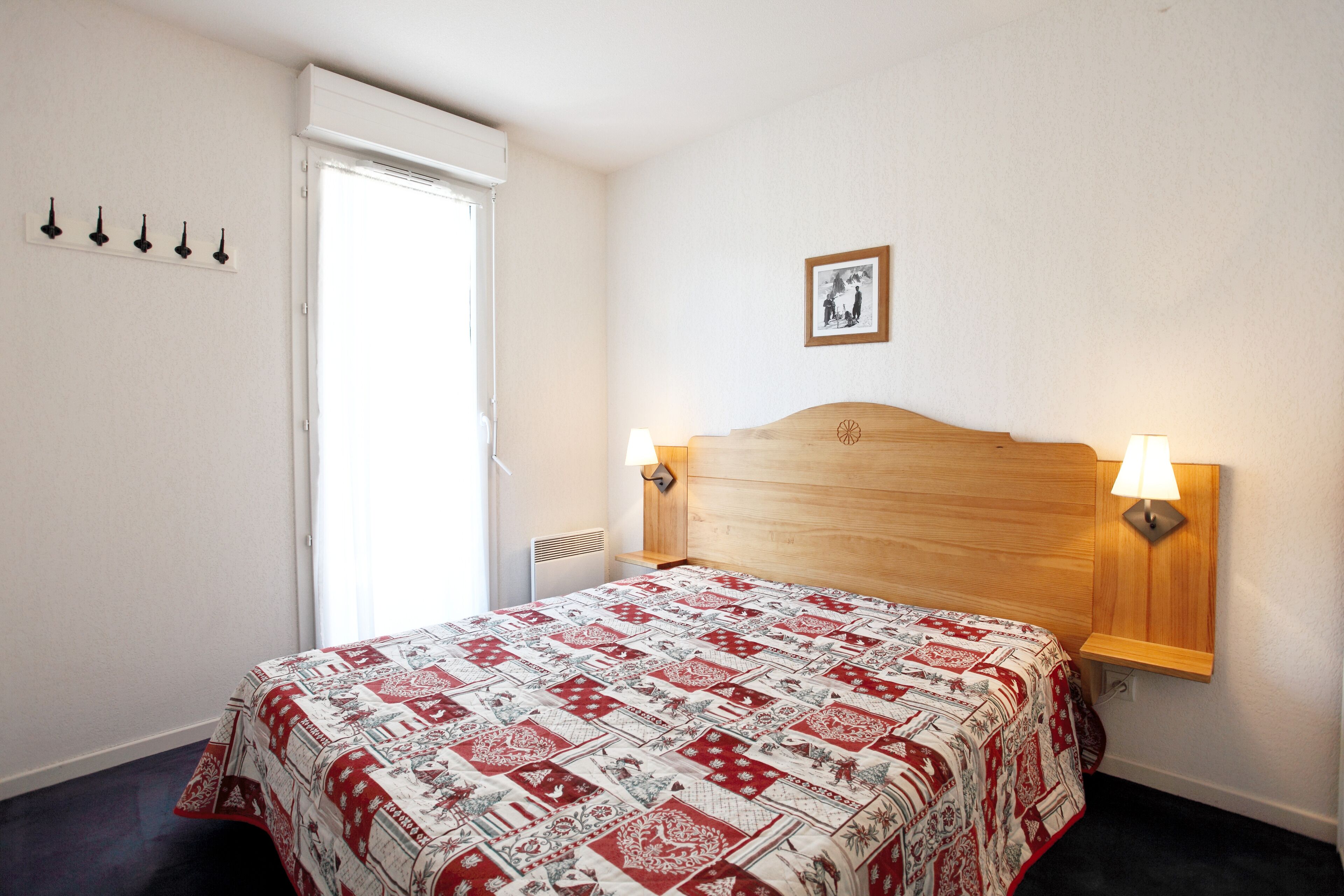 Une chambre à coucher avec une tête de lit en bois, une couvre-lit matelassée, deux lampes de chevet, un tableau au mur et une fenêtre avec un rideau.