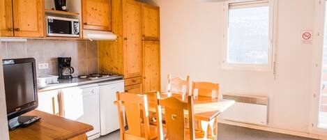 A compact kitchen with wooden cabinets, a microwave, a coffee maker, a stove, and a dining table with chairs.