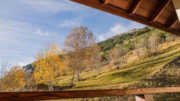 Una terraza de madera con vistas a un paisaje montañoso y árboles de tonos otoñales.