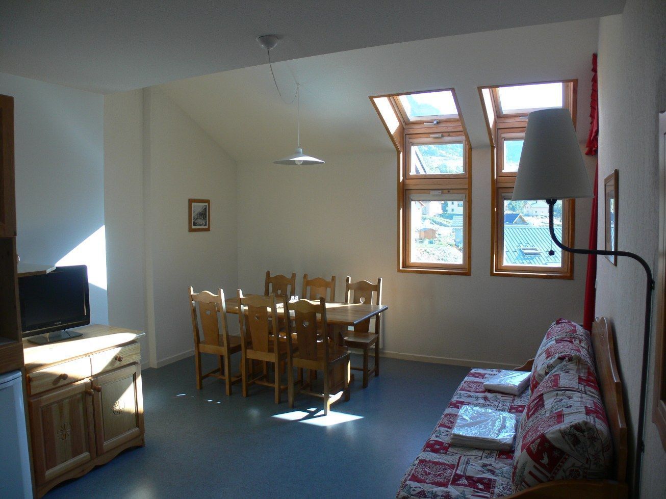 A room with a dining table and chairs, a sofa, a TV on a cabinet, and skylights.
