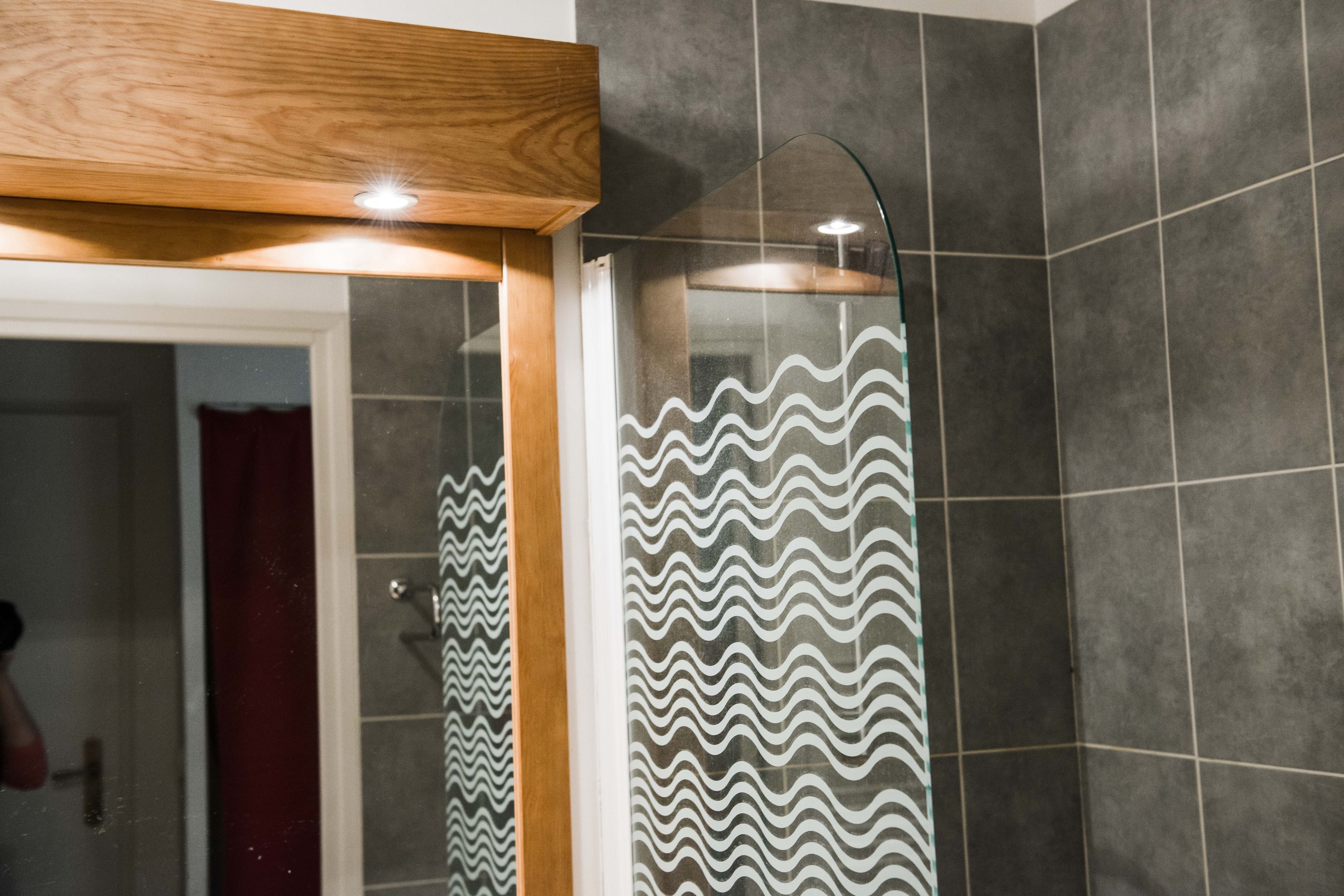 Une salle de bain avec un espace douche, des murs carrelés et une structure de plafond en bois.