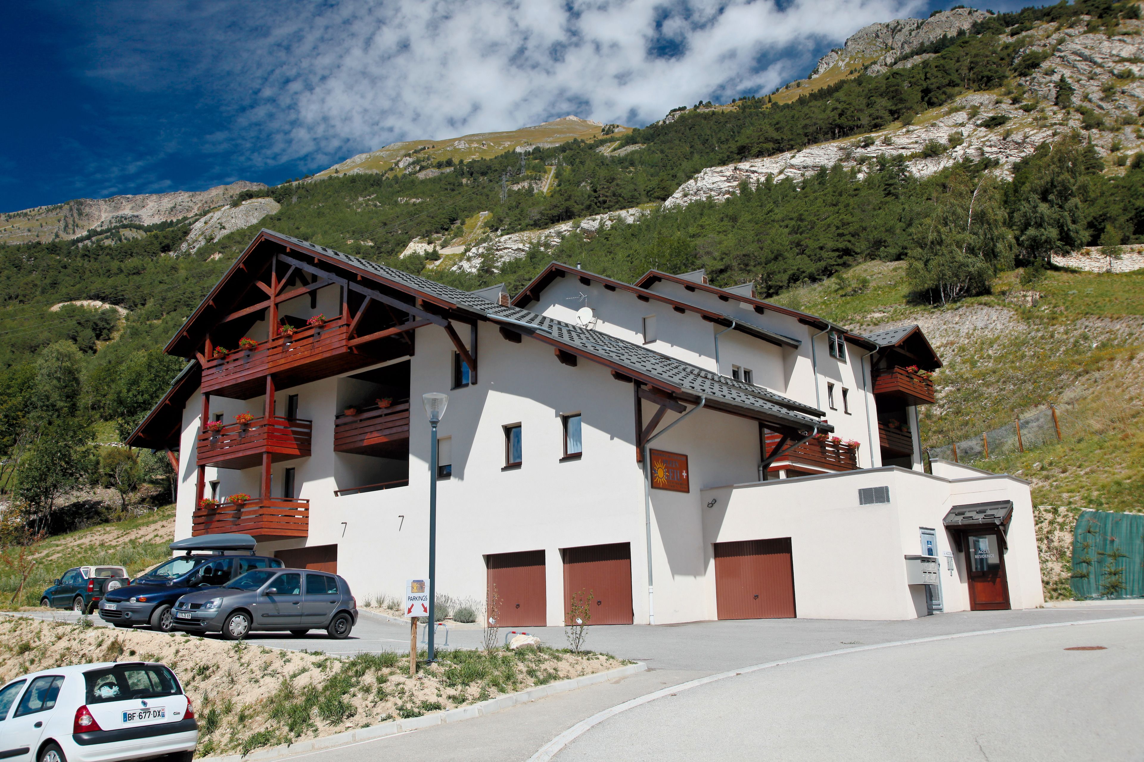 A two-story building with a balcony, a garage, and a mountain backdrop.