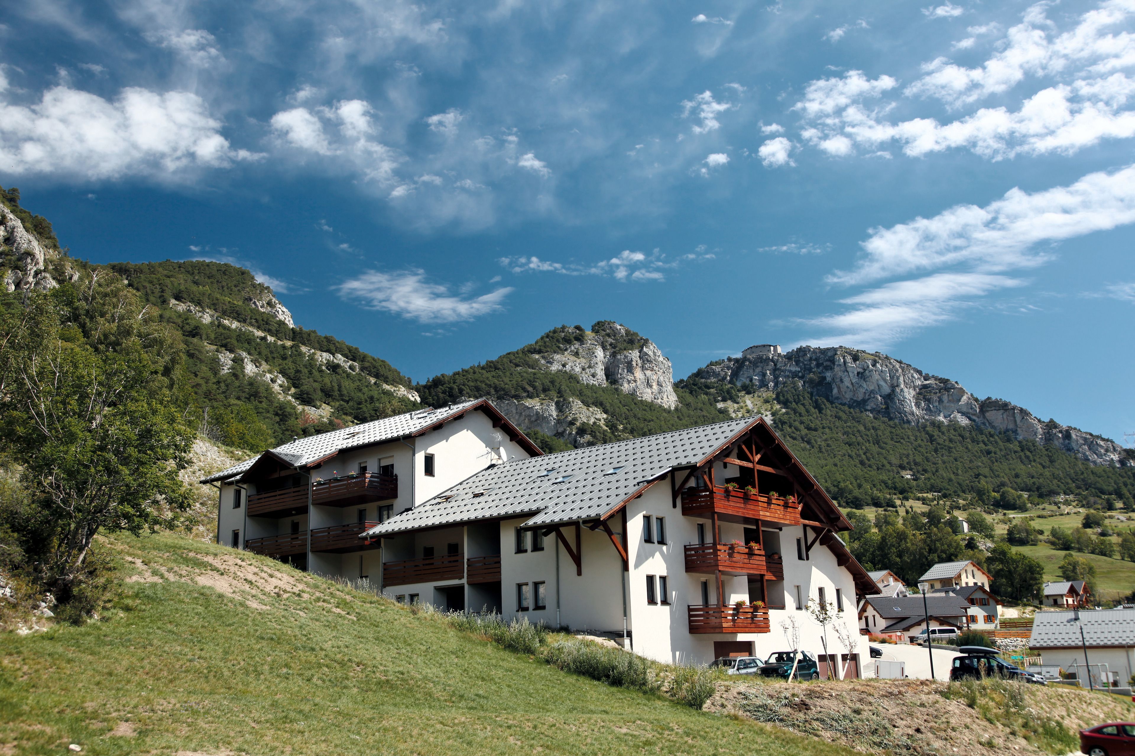 A hillside chalet with multiple balconies, surrounded by lush greenery and mountains.