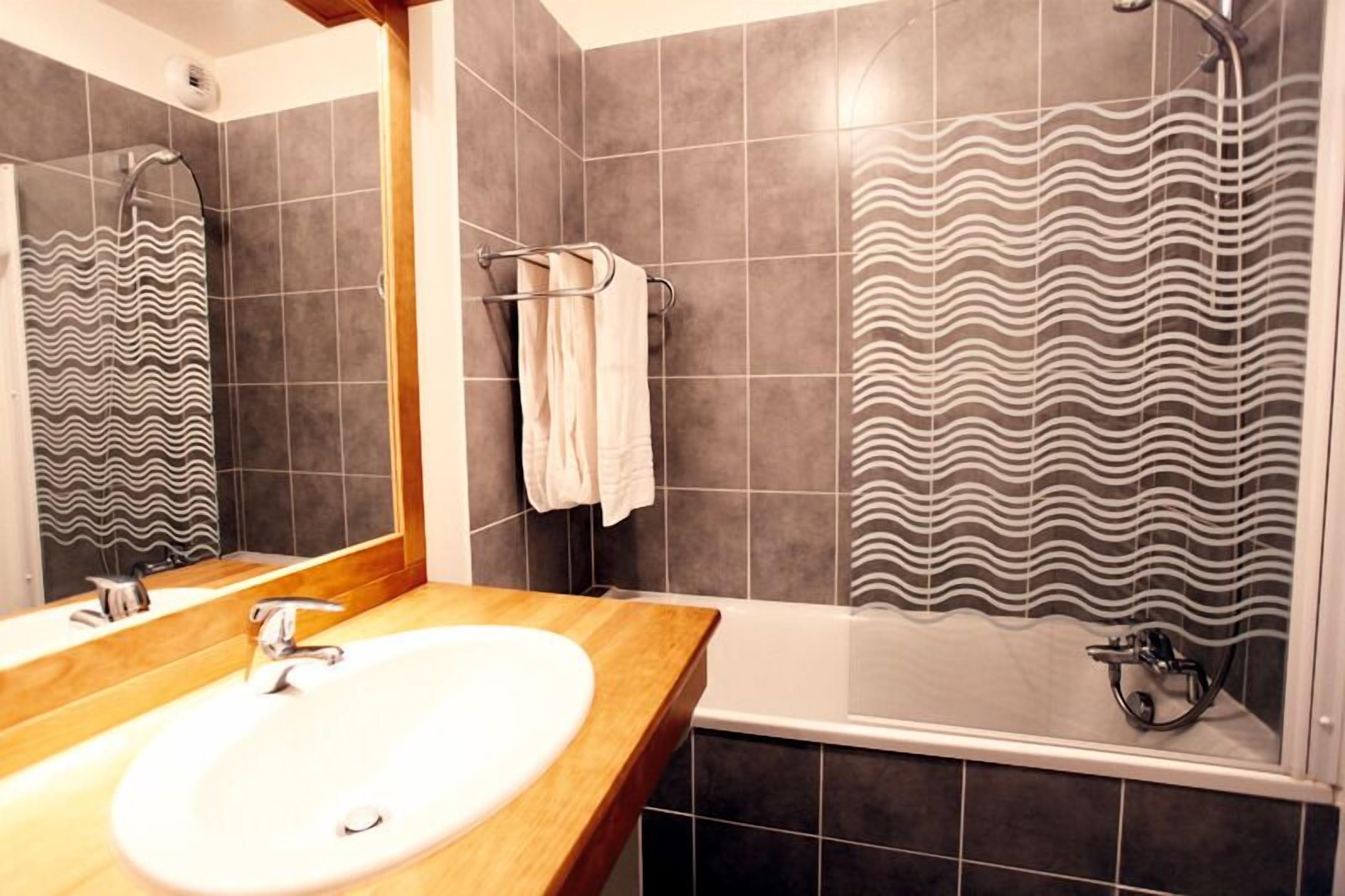 A bathroom with a wooden vanity, a white sink, a towel rack, and a shower with a wavy pattern.