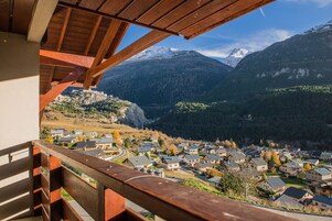 Un balcon offrant une vue sur un village de montagne et sur des sommets enneigés.