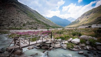 Un puente de madera cruza un río caudaloso, rodeado de terreno rocoso y montañas.