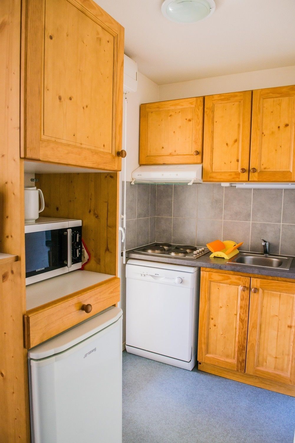 A compact kitchen with wooden cabinets, a microwave, a stove, and a dishwasher.