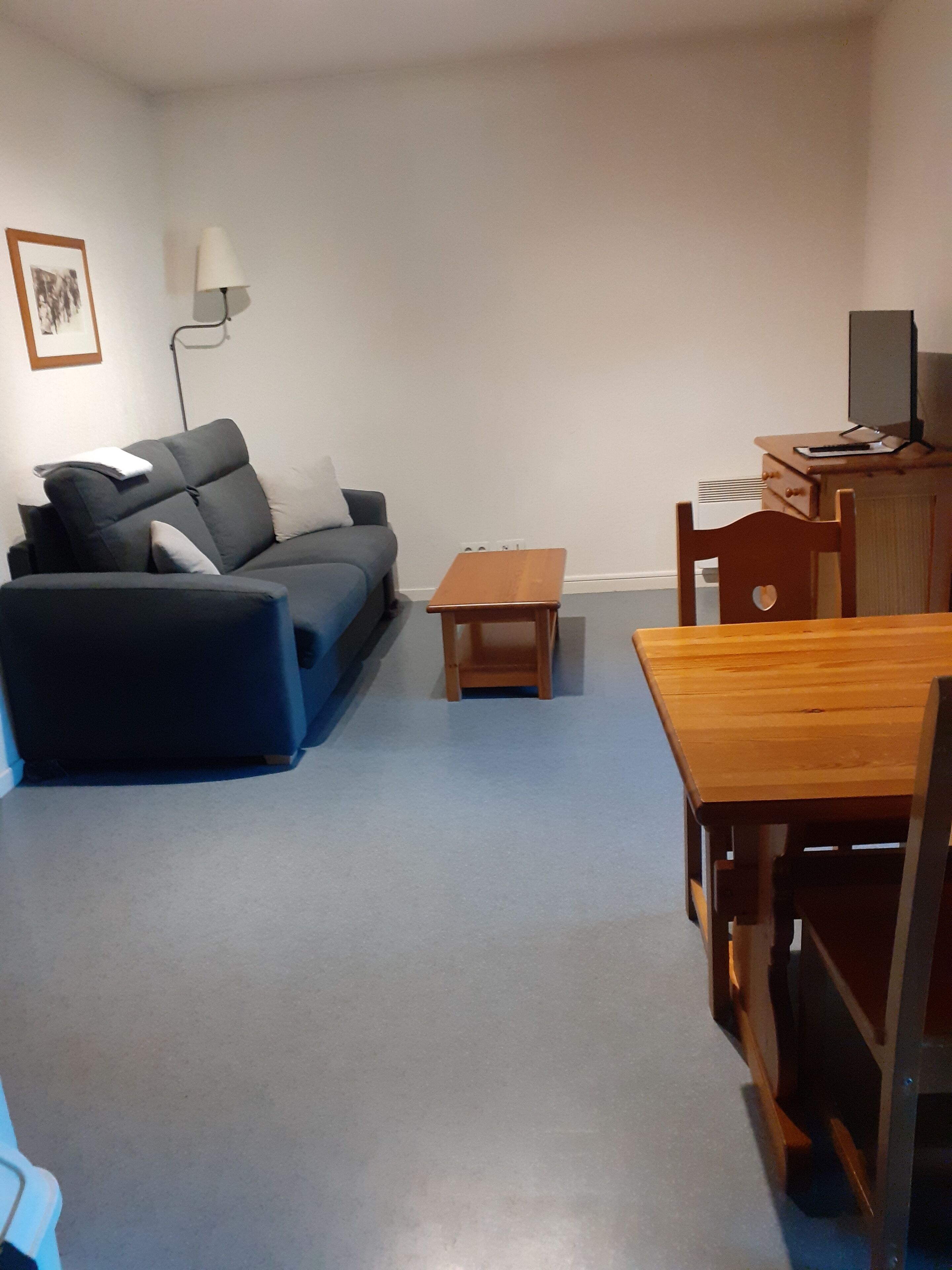 Una sala de estar con un sofá gris, una pequeña mesa de madera y una mesa de comedor de madera con sillas.