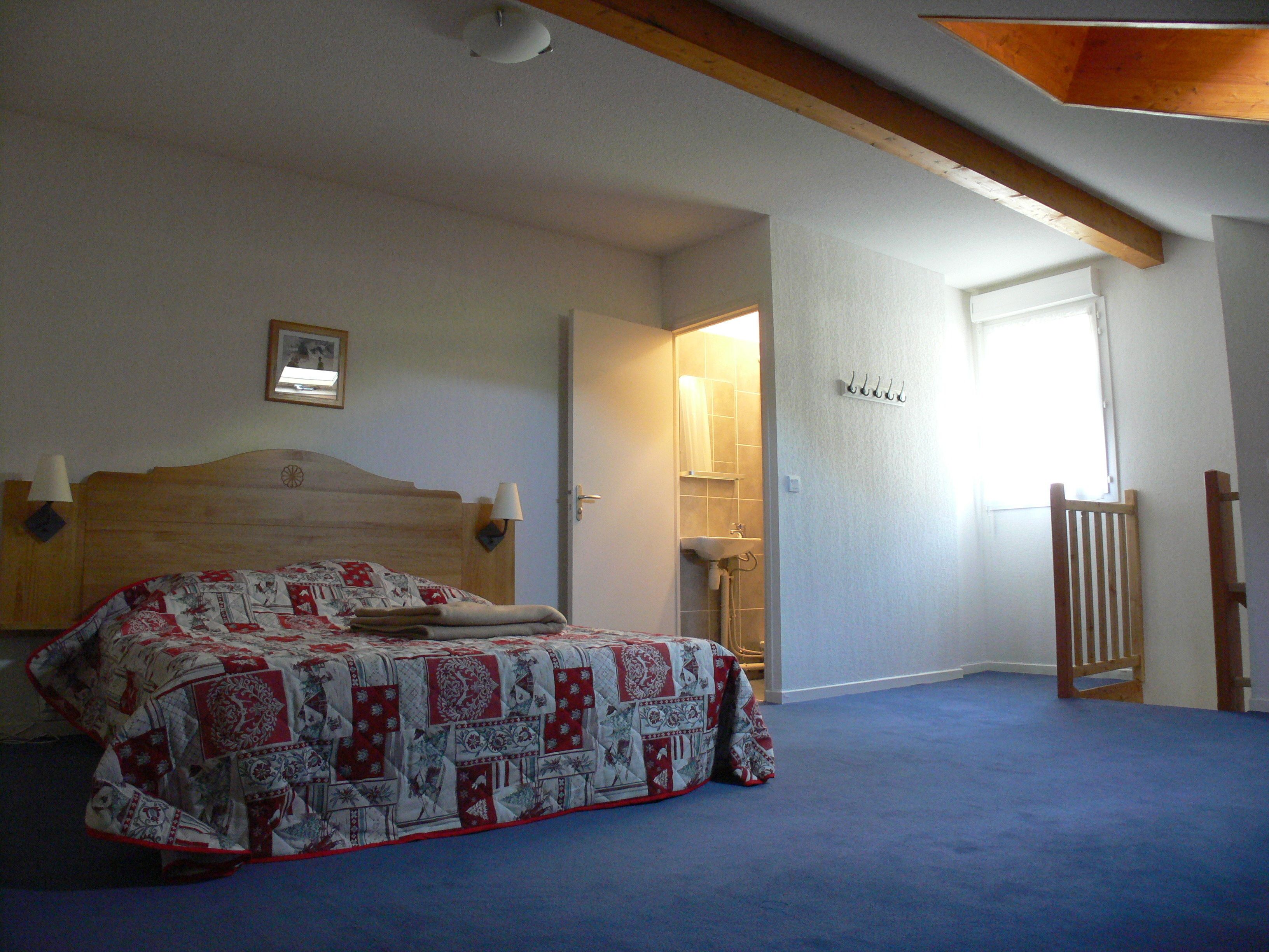A bedroom with a bed, a nightstand, a wall-mounted lamp, and a door leading to a bathroom.