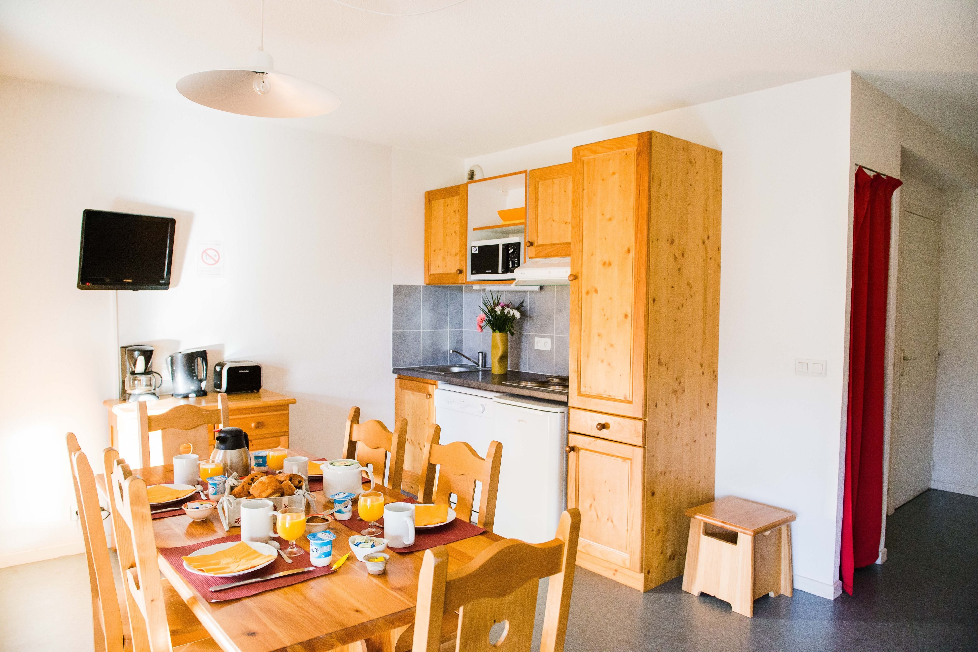 Una cocina compacta con armarios de madera, una mesa de comedor lista para el desayuno y un taburete pequeño.