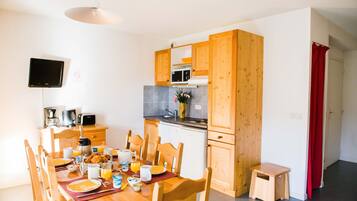 Una cocina compacta con armarios de madera, una mesa de comedor lista para el desayuno y un taburete pequeño.