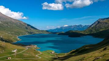 A panoramic view of a mountainous landscape with a large lake, a winding road, and scattered buildings.
