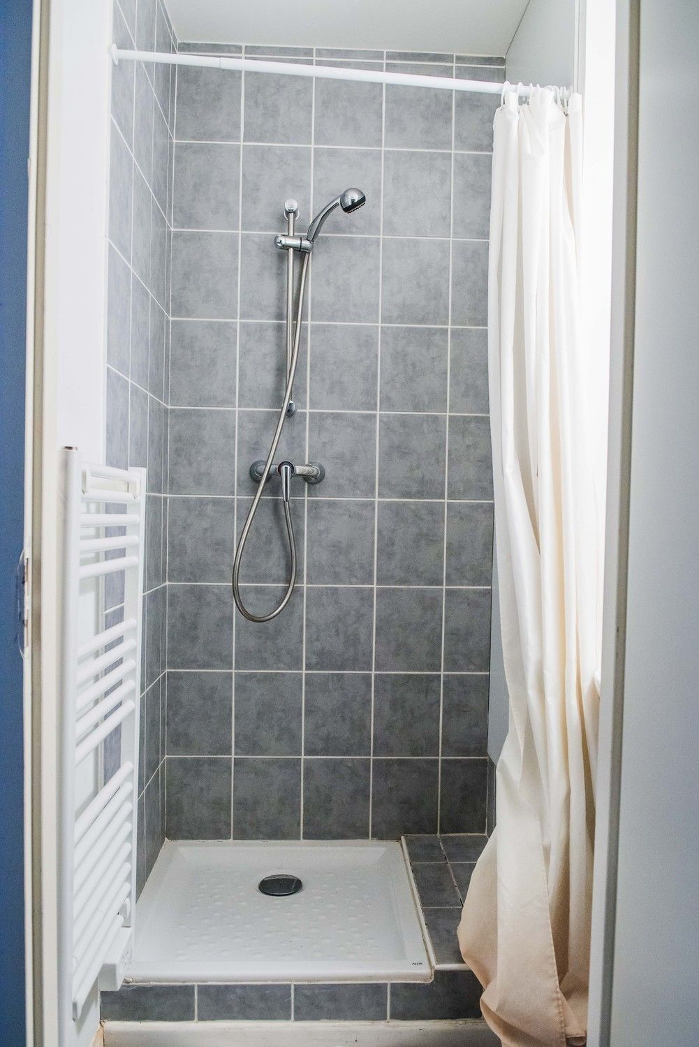 A shower with a white curtain, grey tiles, and a white radiator.