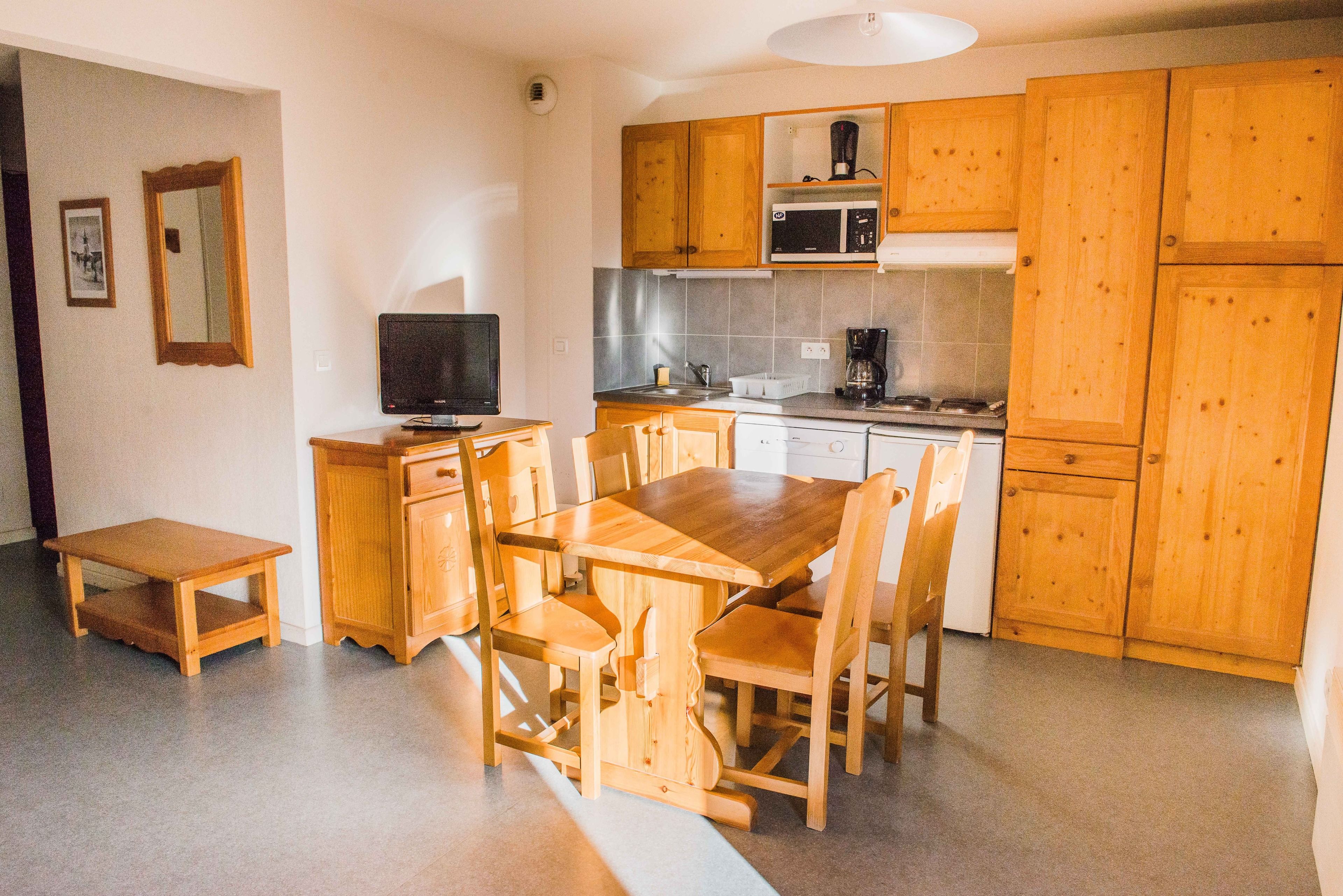 A compact kitchen with wooden cabinets, a dining table, and a television.