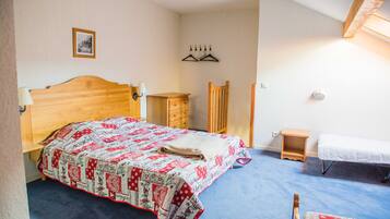 A bedroom with a wooden bed, a small bedside table, a chair, a wardrobe, and a hanging coat rack.