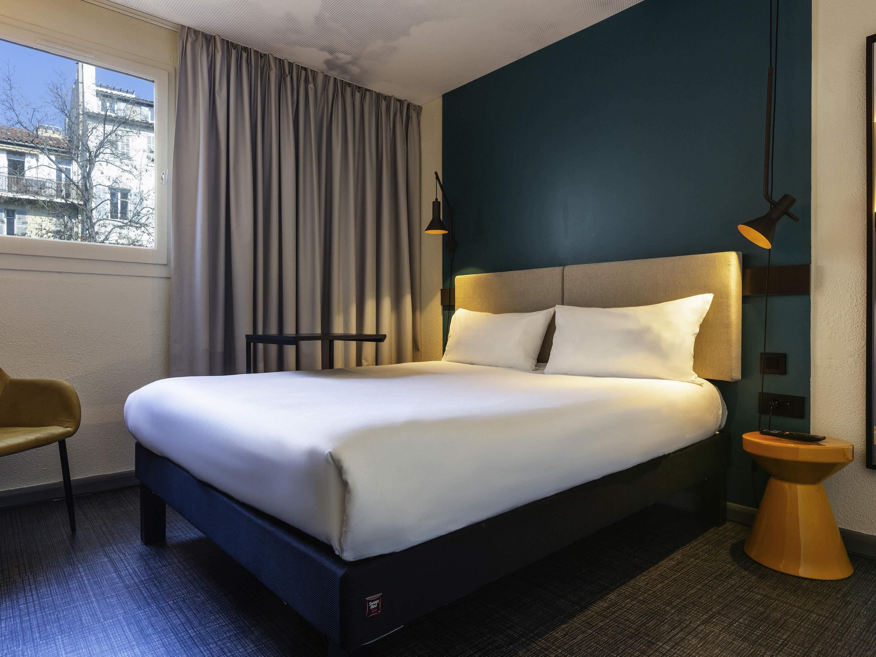 Een hotelkamer met een groot bed, een stoel, een nachtkastje en uitzicht op de stad.