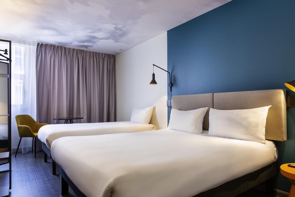 Habitación de hotel con dos camas, un escritorio, una silla y una ventana con cortinas.