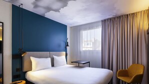 A hotel room with a large bed, a bedside table, a chair, a lamp, and a window with curtains. - Ibis Marseille Centre Préfecture (Marseille)