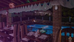 An outdoor dining area with a pool, wicker furniture, and a view of a building in the background. - Anagenessis Village (Zakynthos)