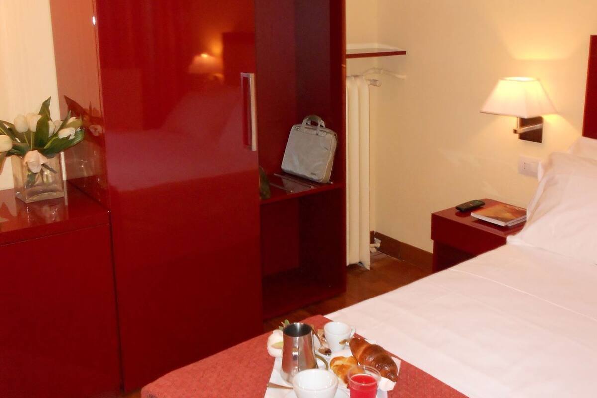A hotel room with a bed, a nightstand, a red wardrobe, and a table with breakfast items.