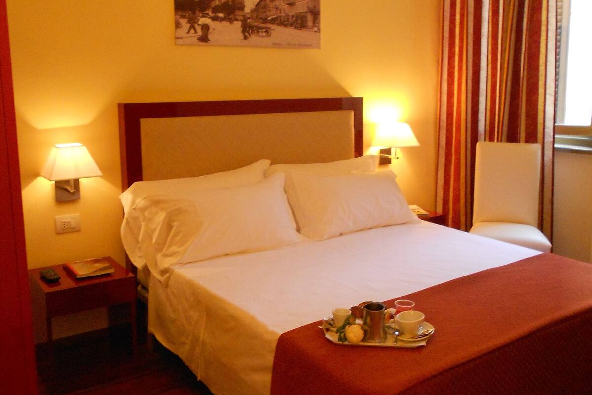 A hotel room with a bed, two bedside lamps, a tray with breakfast items, and a picture on the wall.