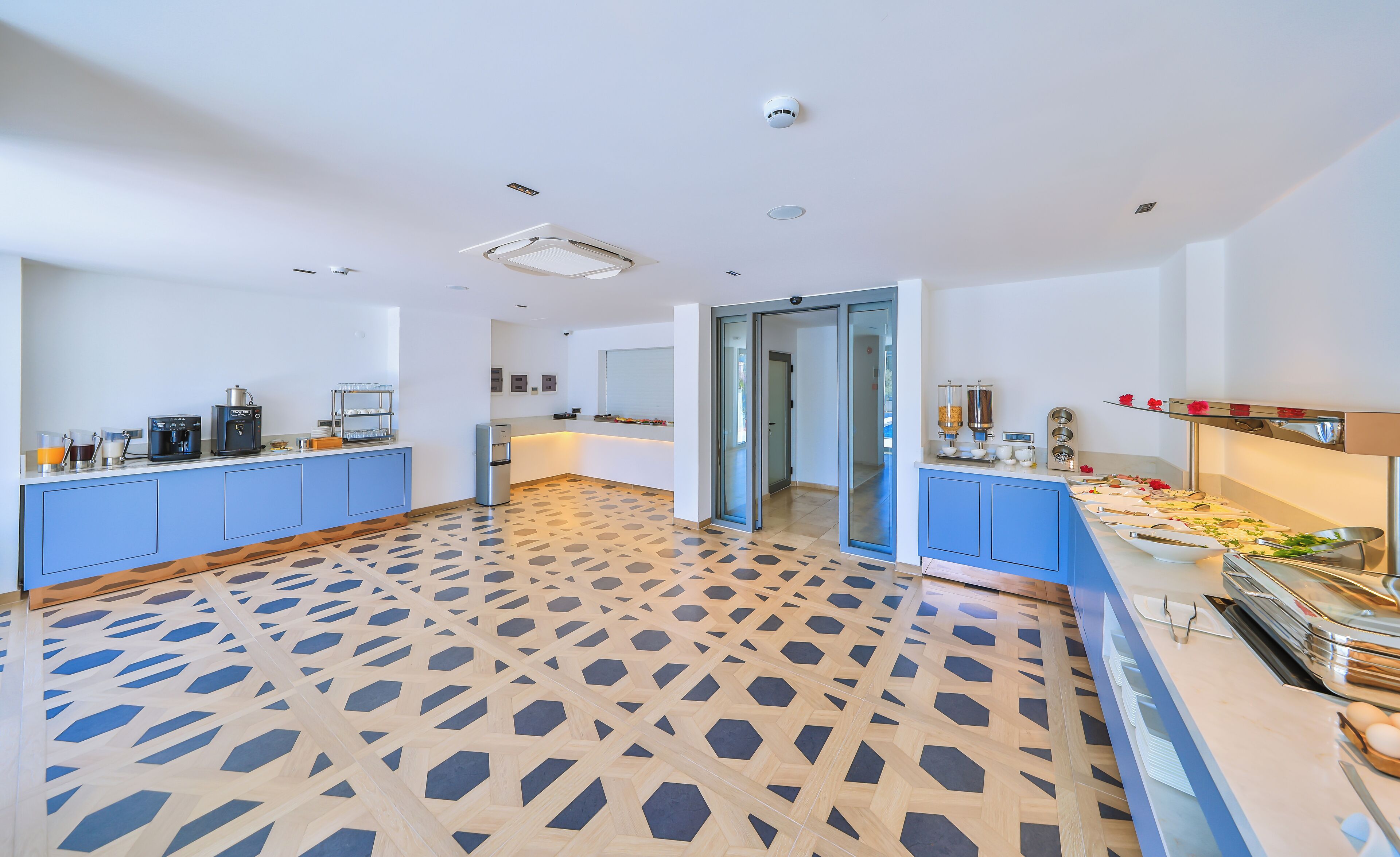 Una habitación amplia con piso estampado, un área para café y una mesa de buffet.