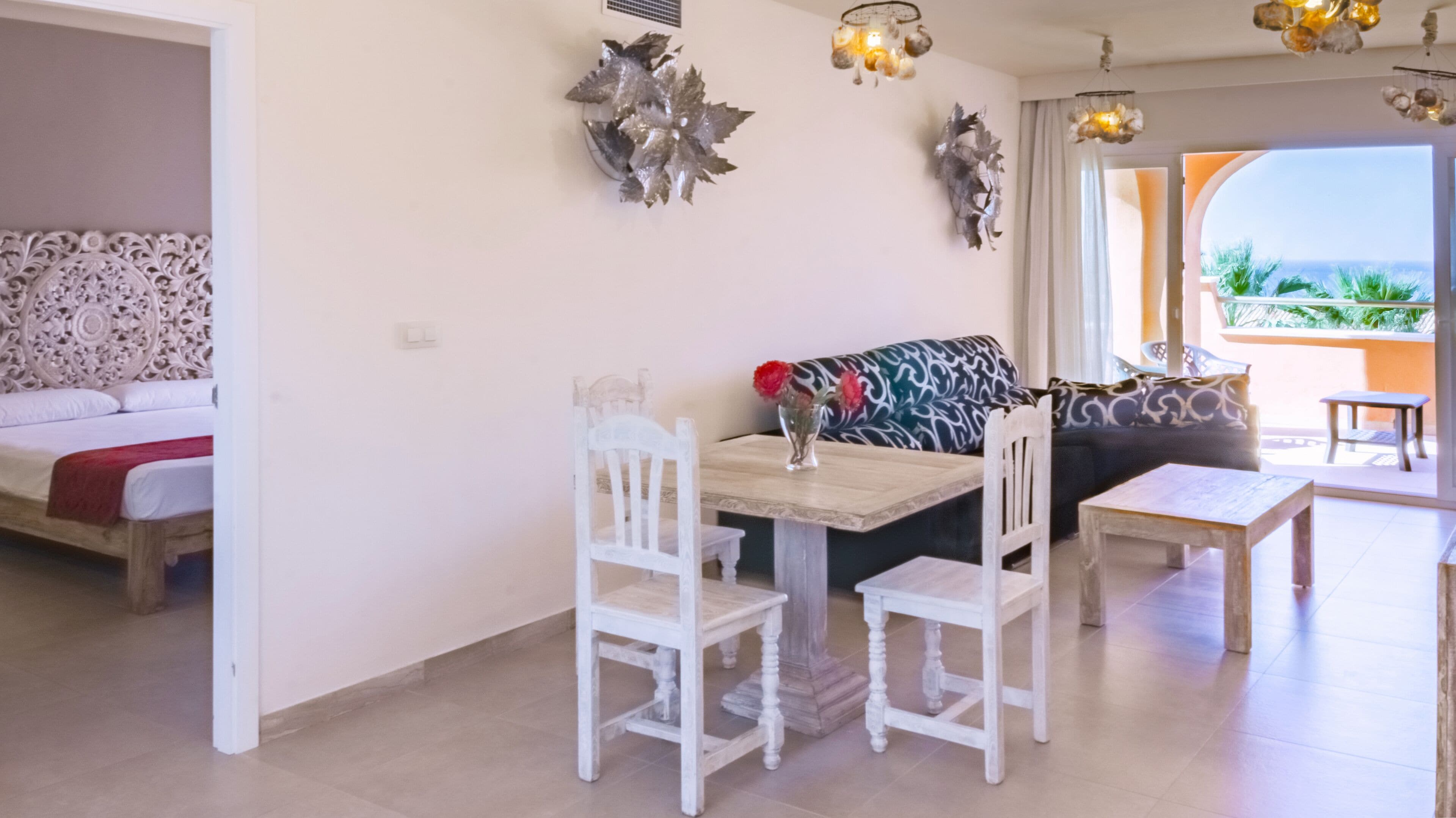 A dining area with a table and chairs, a sofa, decorative wall art, and a view through a glass door.