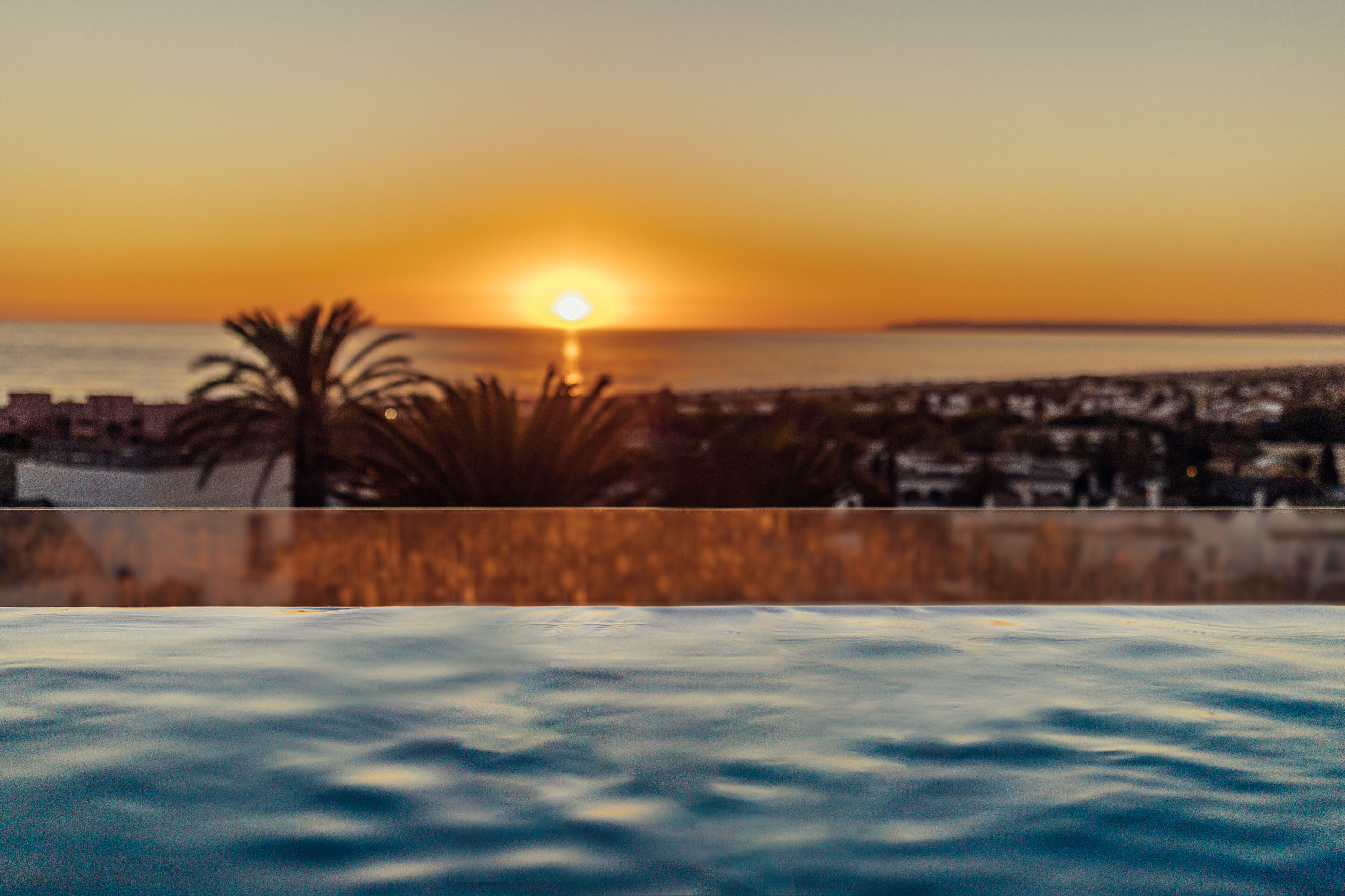 Vista del atardecer desde una zona de piscina con un paisaje urbano al fondo.