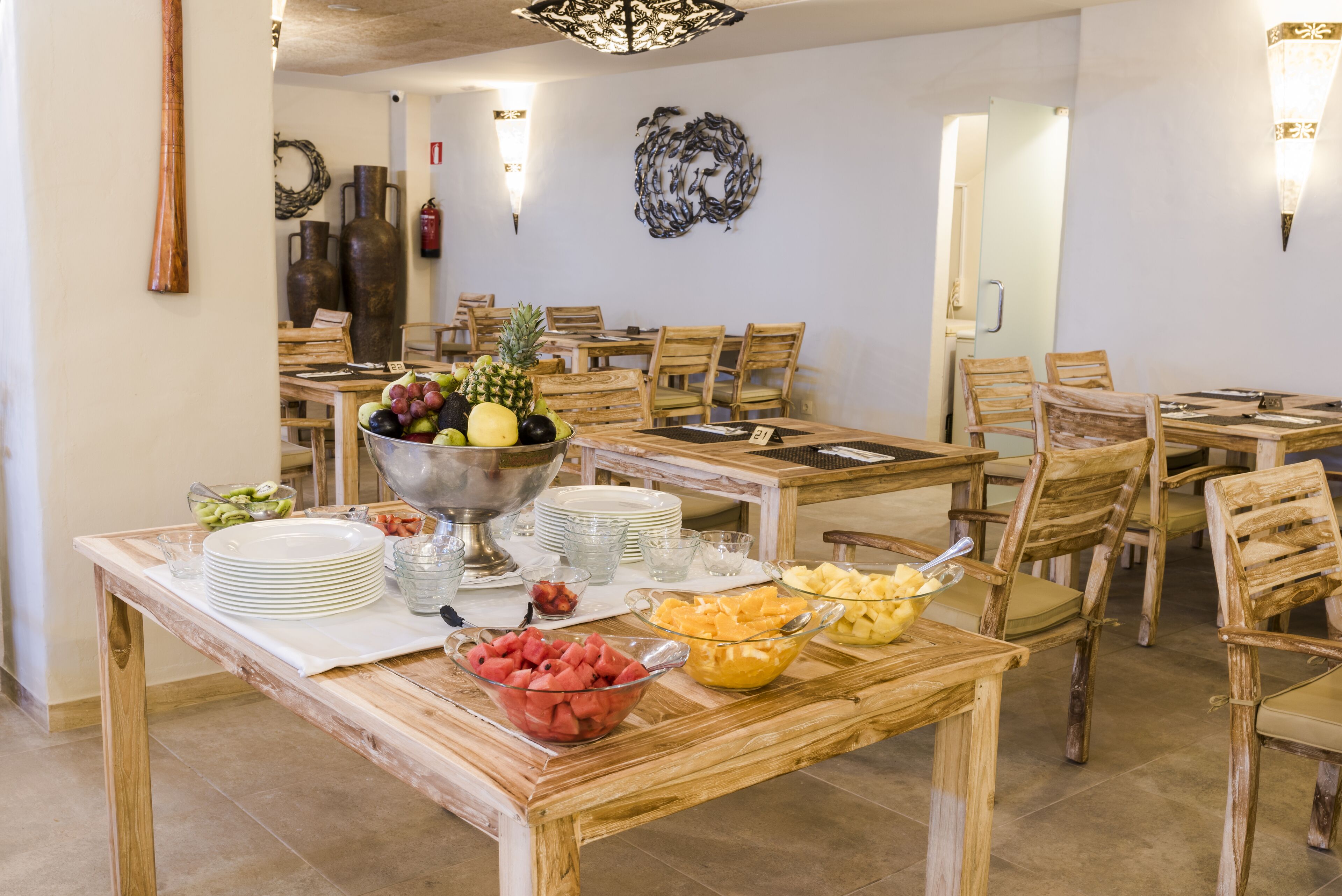 Comedor con mesas y sillas de madera, cuencos de fruta y platos apilados.