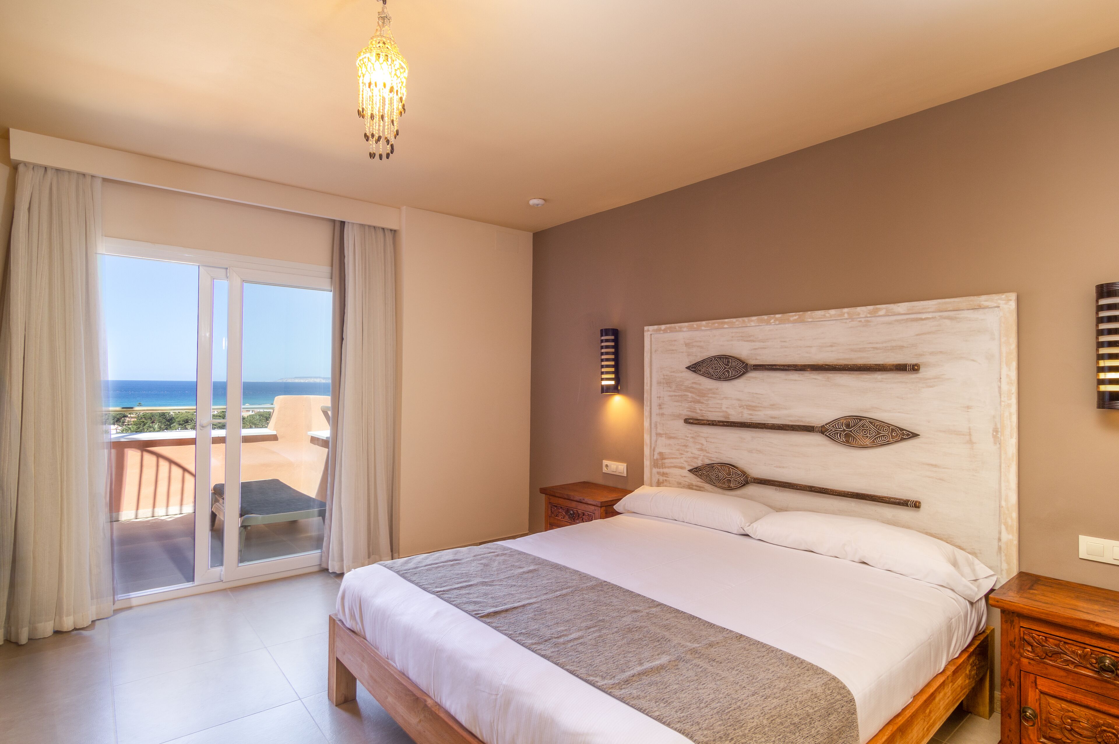 Une chambre avec un grand lit, un balcon avec vue et un lustre.