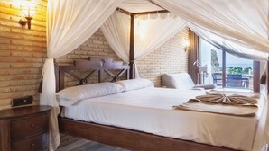 A spacious bedroom with a large bed, a wooden headboard, a nightstand, and a view of the outdoors through a large window. - Hotel El Cortijo De Zahara by Q Hotels (Tarifa)
