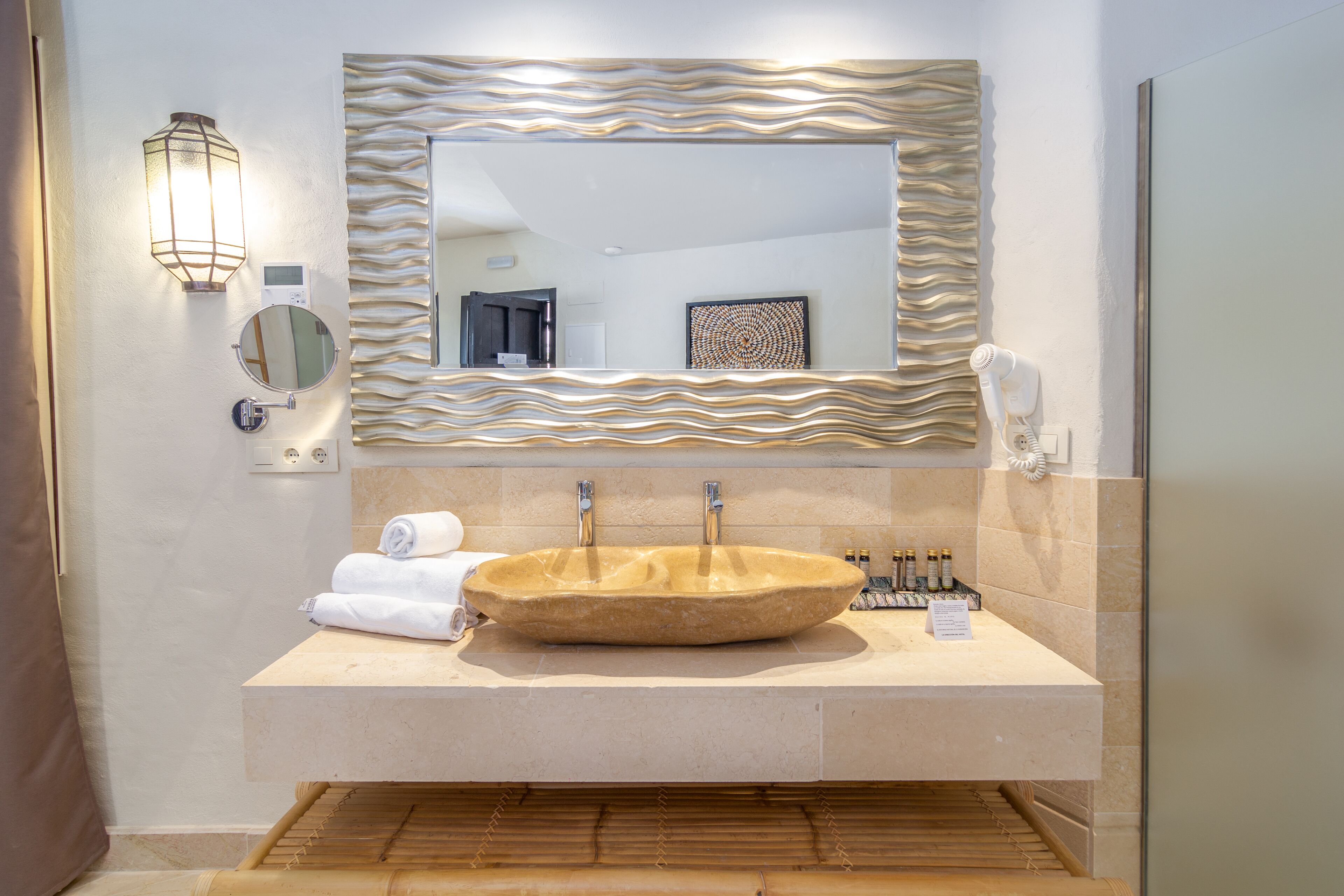 A bathroom with a large, oval sink, a mirror with a wavy frame, a towel rack, and a hairdryer on the counter.