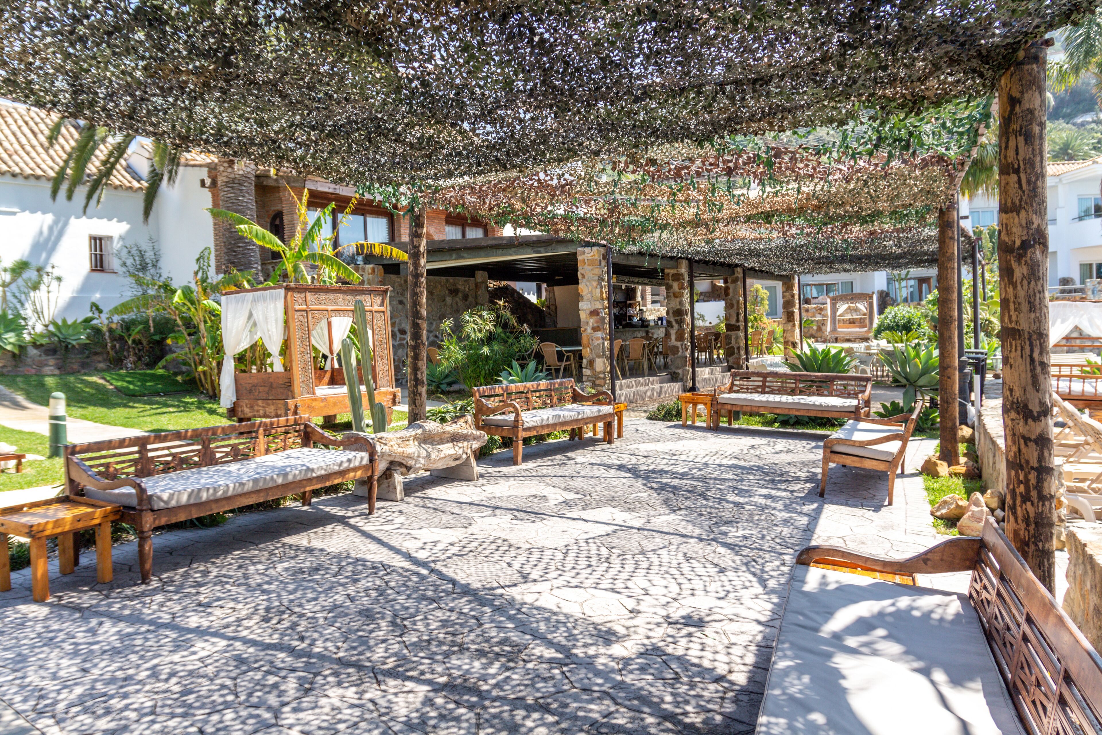 Zona d'estar a l'exterior amb sòl de pedra, bancs de fusta i una pérgola coberta de vïnes.