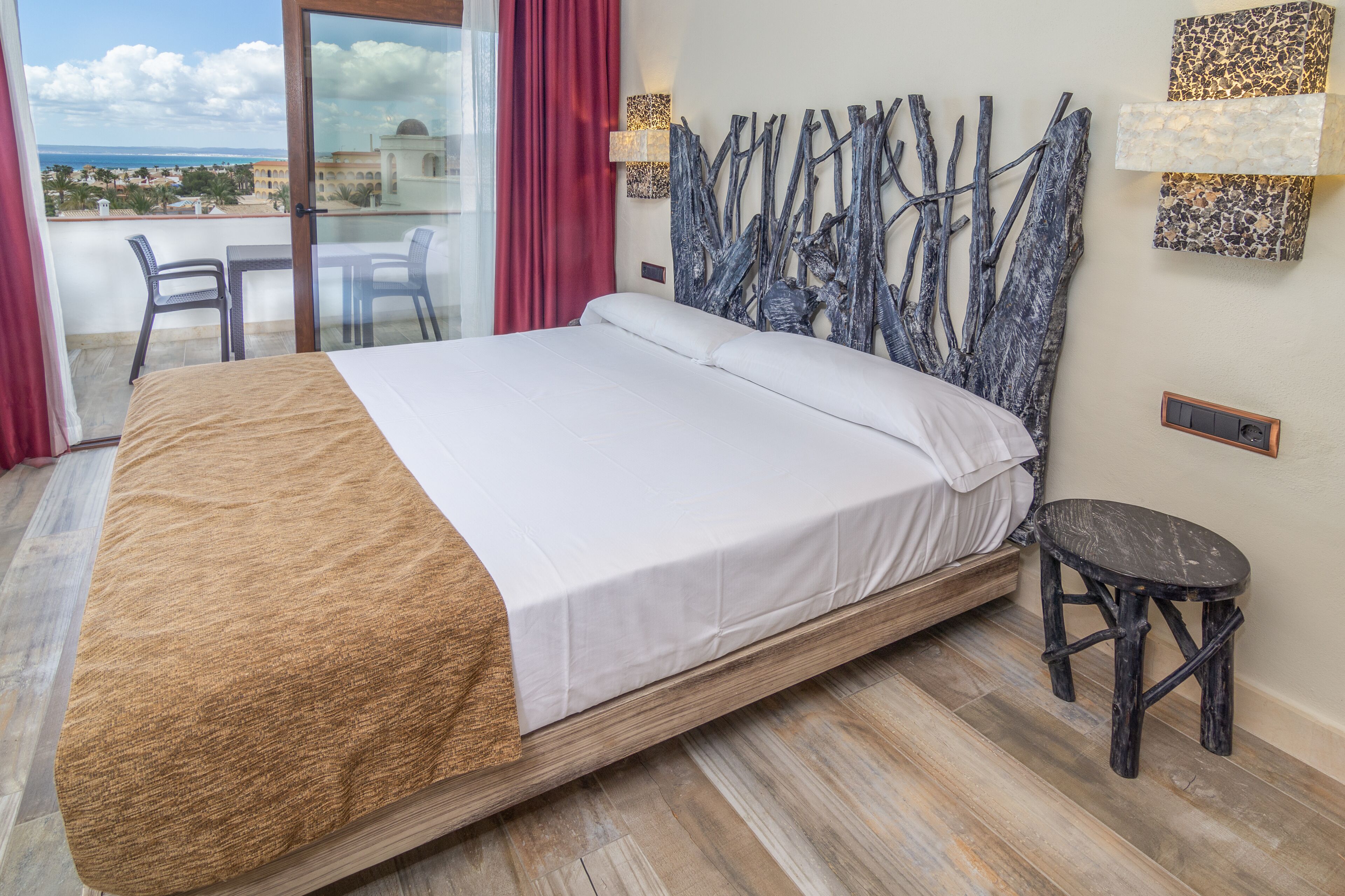 Habitación de hotel con una cama grande, balcón con mesa y sillas, y vista al mar.