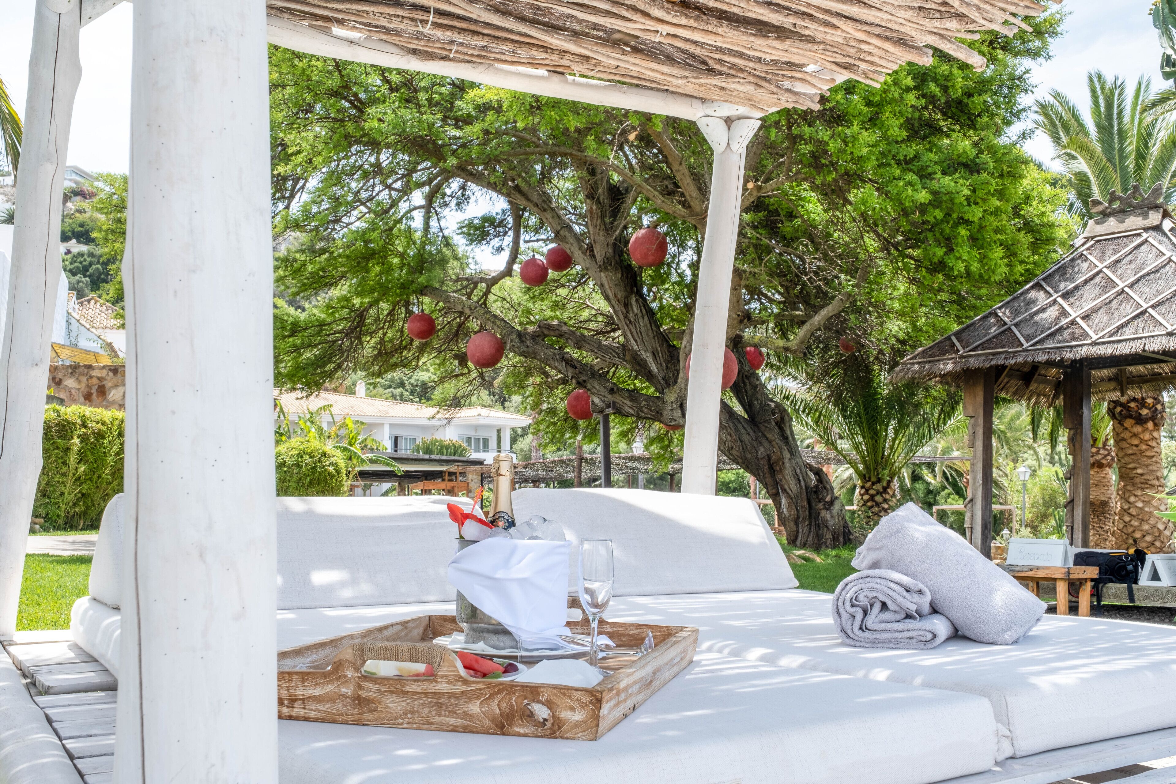 A covered outdoor seating area with a wooden table, a bottle of champagne, and a glass.