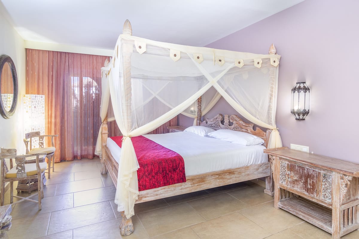 Ein Bett mit Himmelbett, ein Nachttisch aus Holz, ein Sessel und eine Wandlampe.