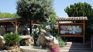 A garden area with a wooden pergola, a rock formation, a small fountain, and a cactus.