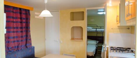 A compact room with a bunk bed, a small kitchenette, a table, and a window with curtains.