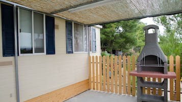 Un patio couvert avec un barbecue, une clôture en bois et une maison avec des volets.