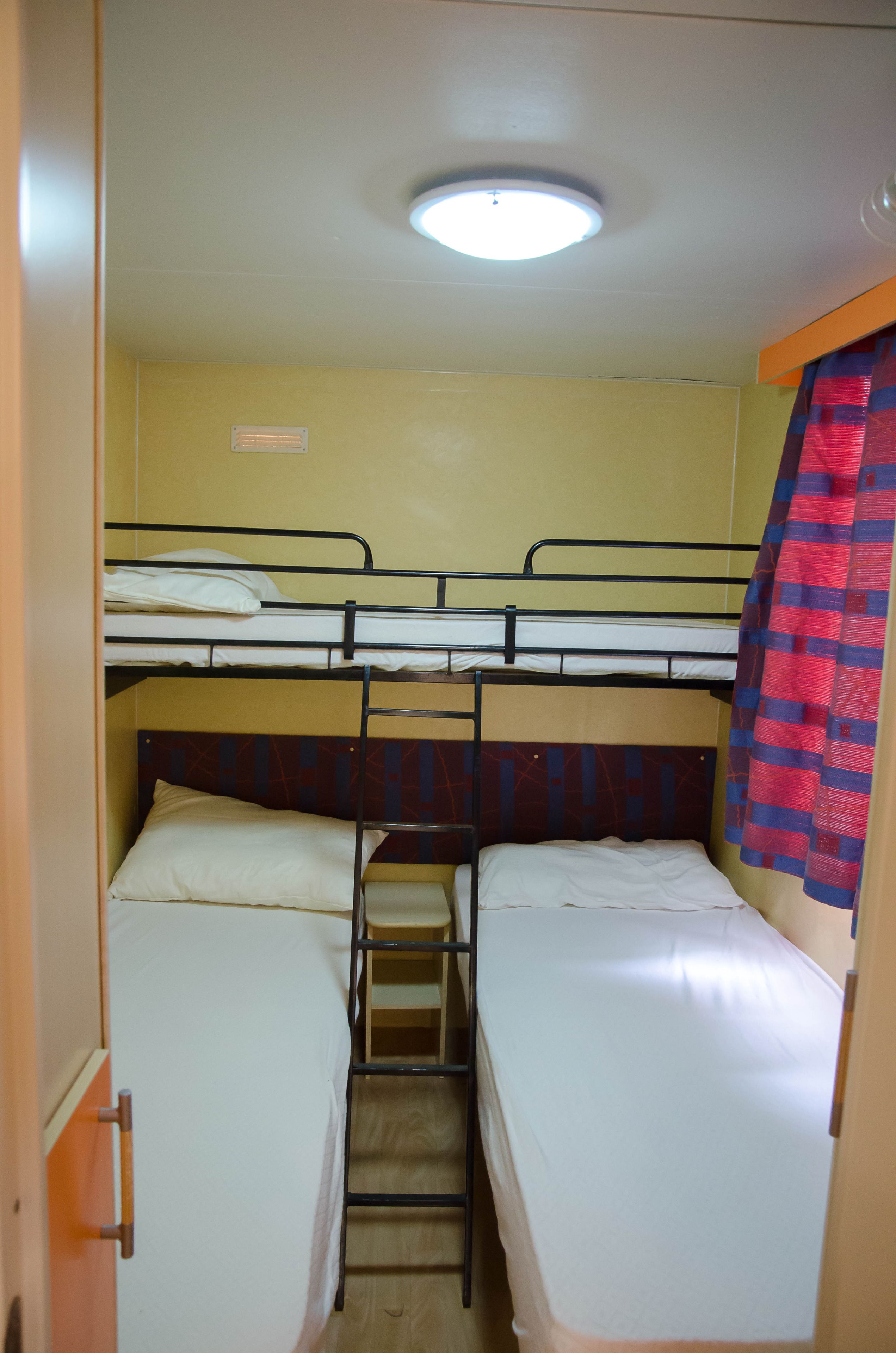 Ein Schlafzimmer mit Etagenbett, einer Stehleiter, einer Deckenleuchte und einem Vorhang.