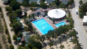 An aerial view of a resort with two swimming pools, a large circular building, and surrounding palm trees.