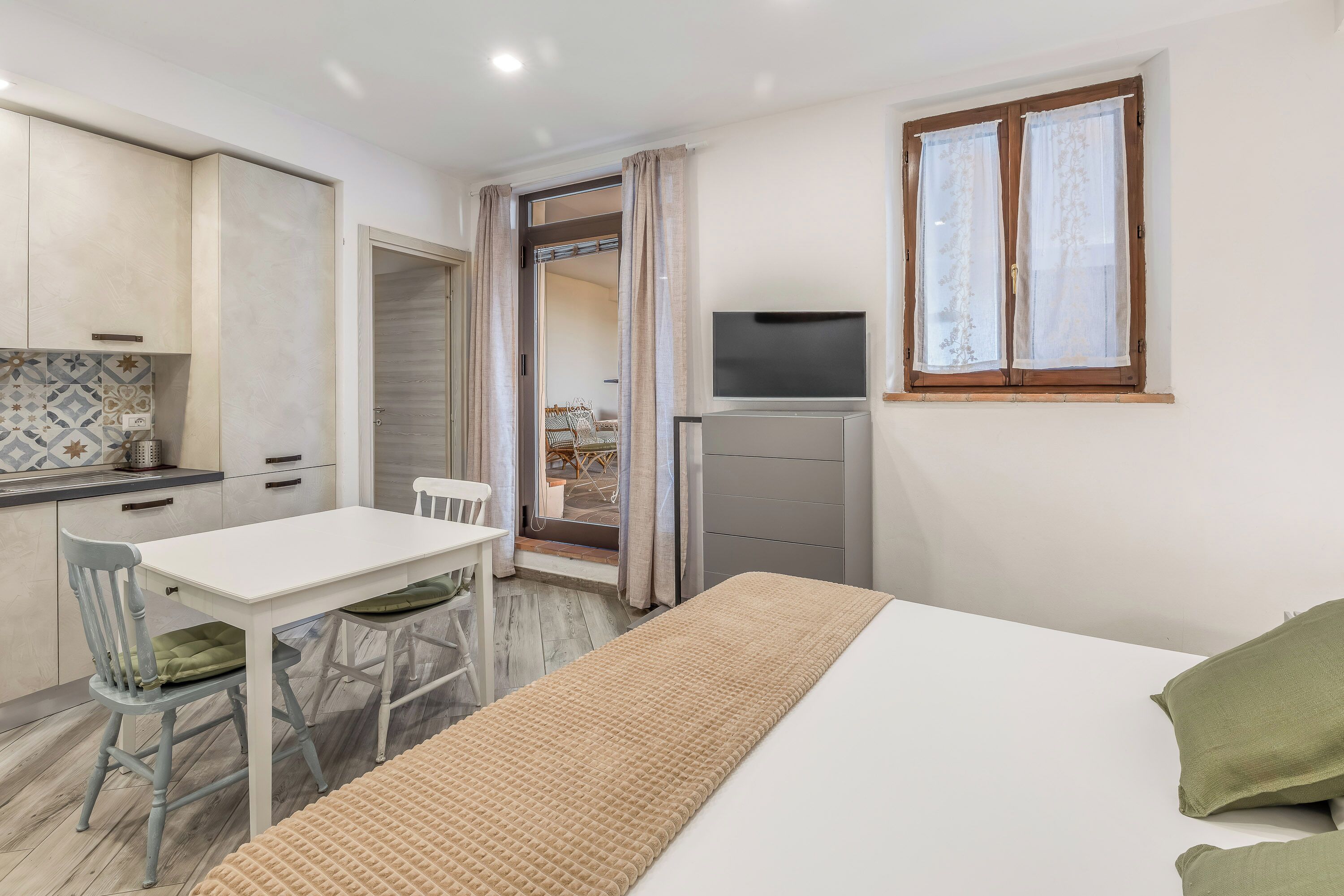 Una habitación compacta con cama, televisor, mesa de comedor con sillas y kitchenette.