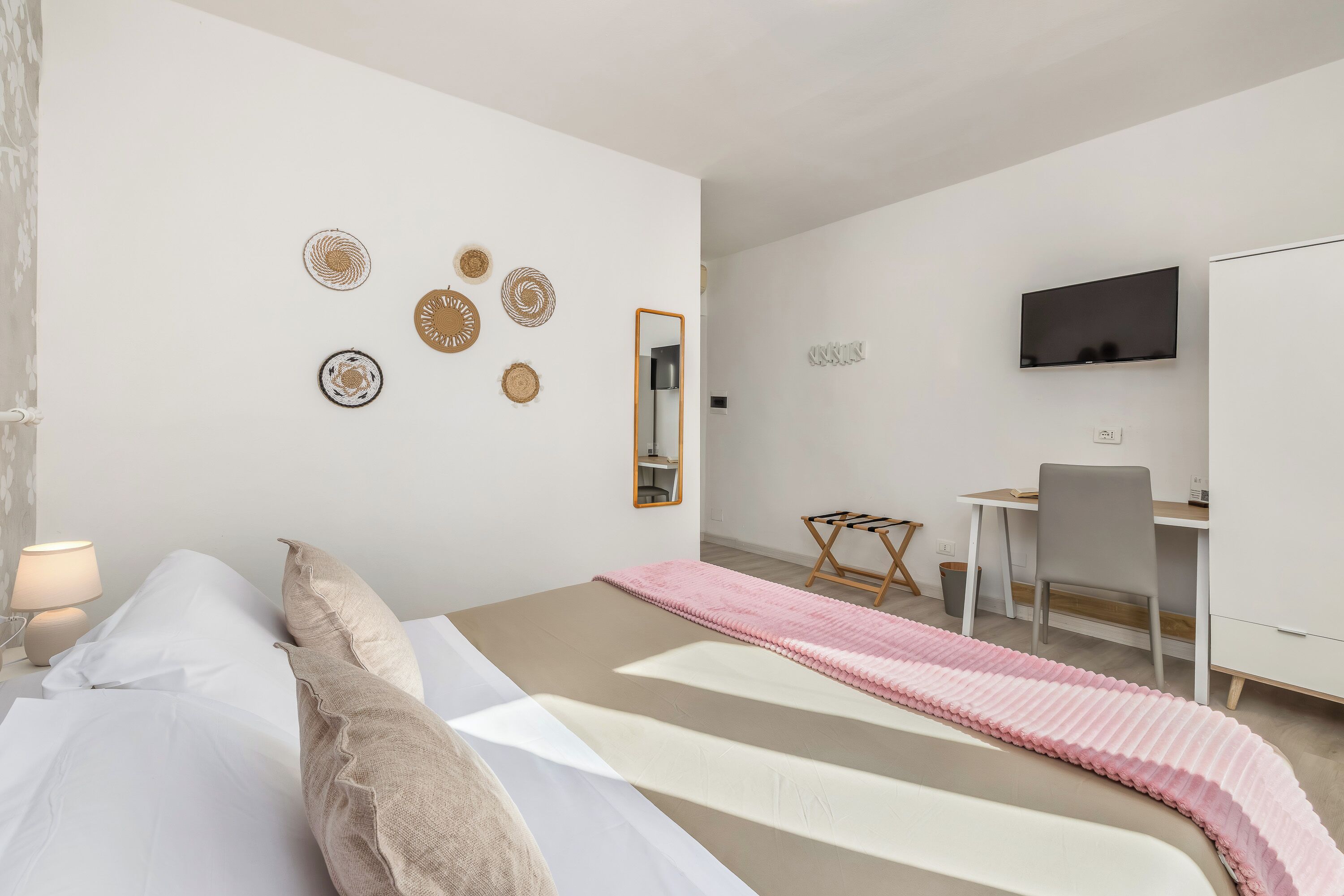 Un dormitorio con cama, mesita de noche, lámpara, decoración en la pared, un escritorio, silla y televisor.