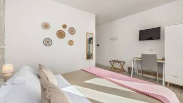 Un dormitorio con cama, mesita de noche, lámpara, decoración en la pared, un escritorio, silla y televisor.