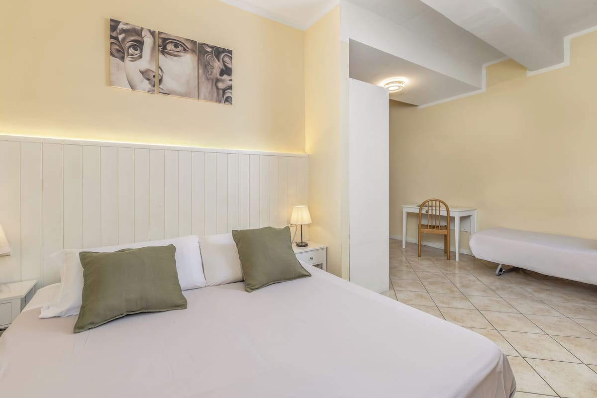 A hotel room with a bed, a nightstand with a lamp, a chair, and a bench.